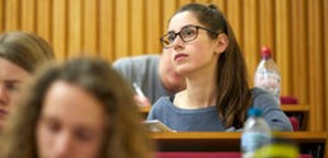 Students sitting in tiered seating taking notes and listening attentively in a lecture. 